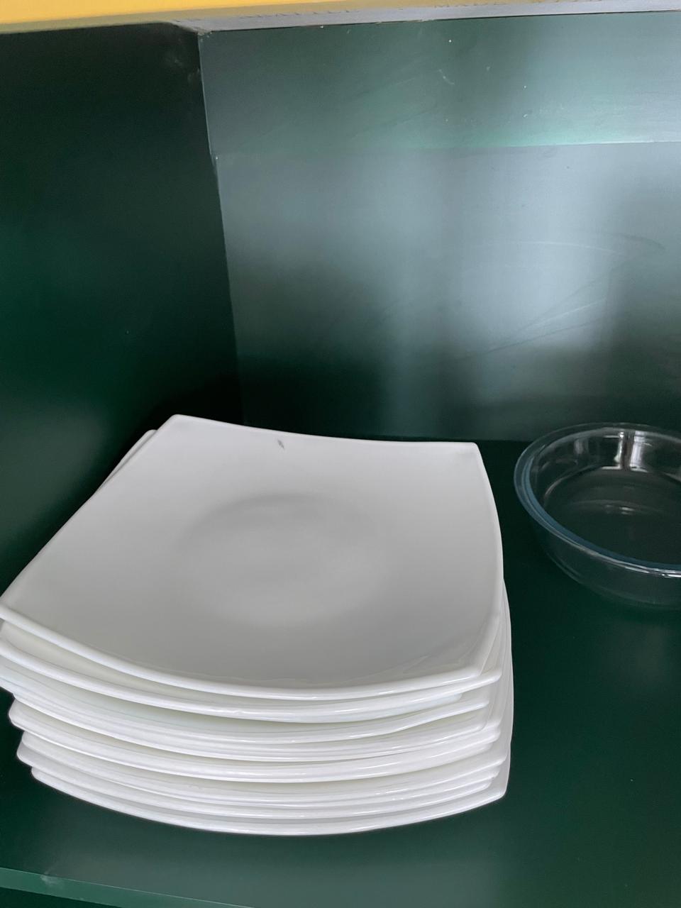 Stack of white square dinner plates with a glass serving bowl